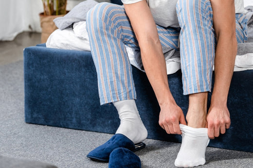 A man is sitting on a bed and putting on white sports ankle socks