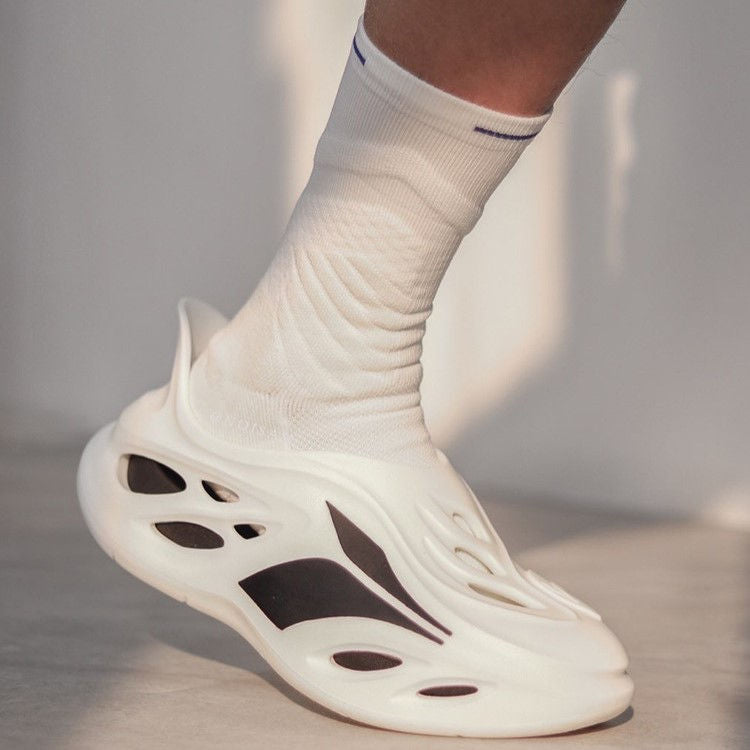 Close-up of a foot in a white futuristic sneaker with cut-out details, paired with a white basketball sock with a blue stripe.