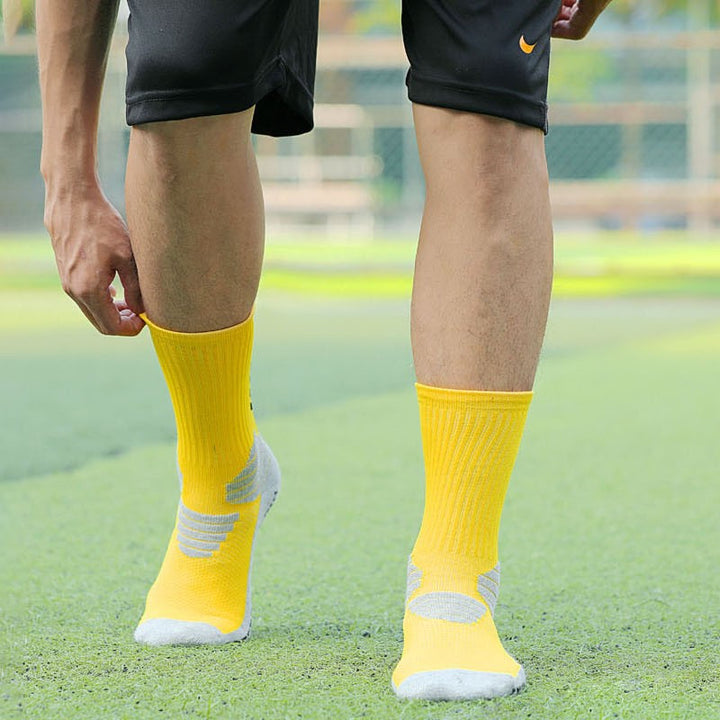 Athlete standing on a turf field, showcasing bright yellow basketball socks with strategic gray cushioning on the soles and ankles for enhanced performance and support.