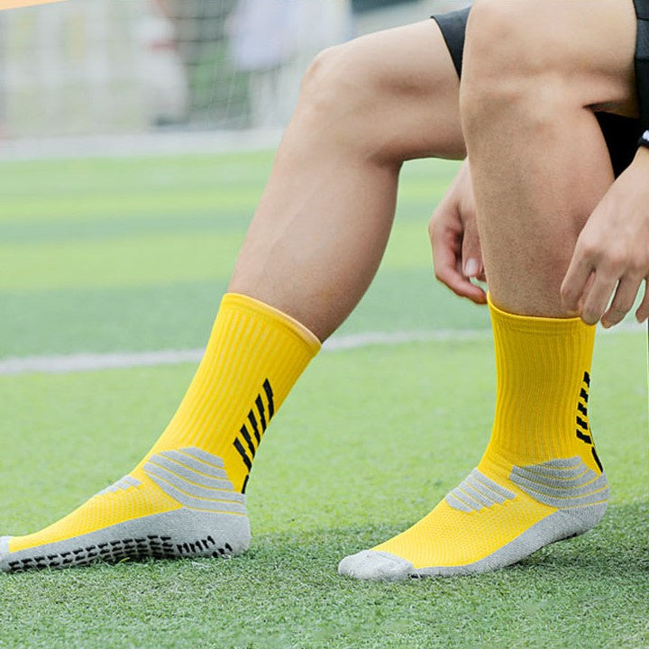 Athlete sitting on a grass field wearing bright yellow basketball socks with gray cushioned areas on the soles and ankles, designed for performance and comfort.