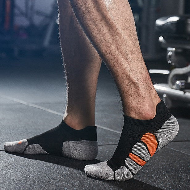 Man wearing black and gray ankle socks with orange accents in a gym setting.