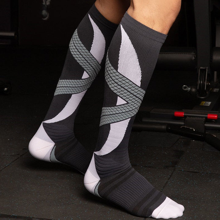 Person wearing a pair of black compression socks with grey and white geometric patterns in a gym setting