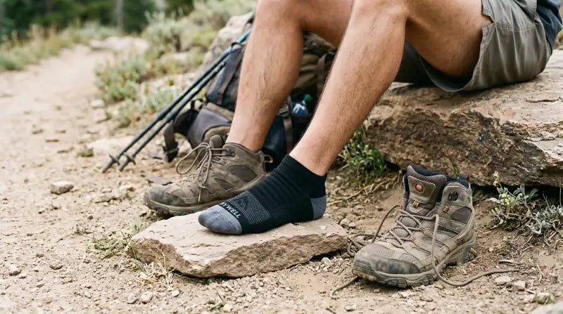 Hiker resting with a boot off and a black and gray ankle sock on a rock